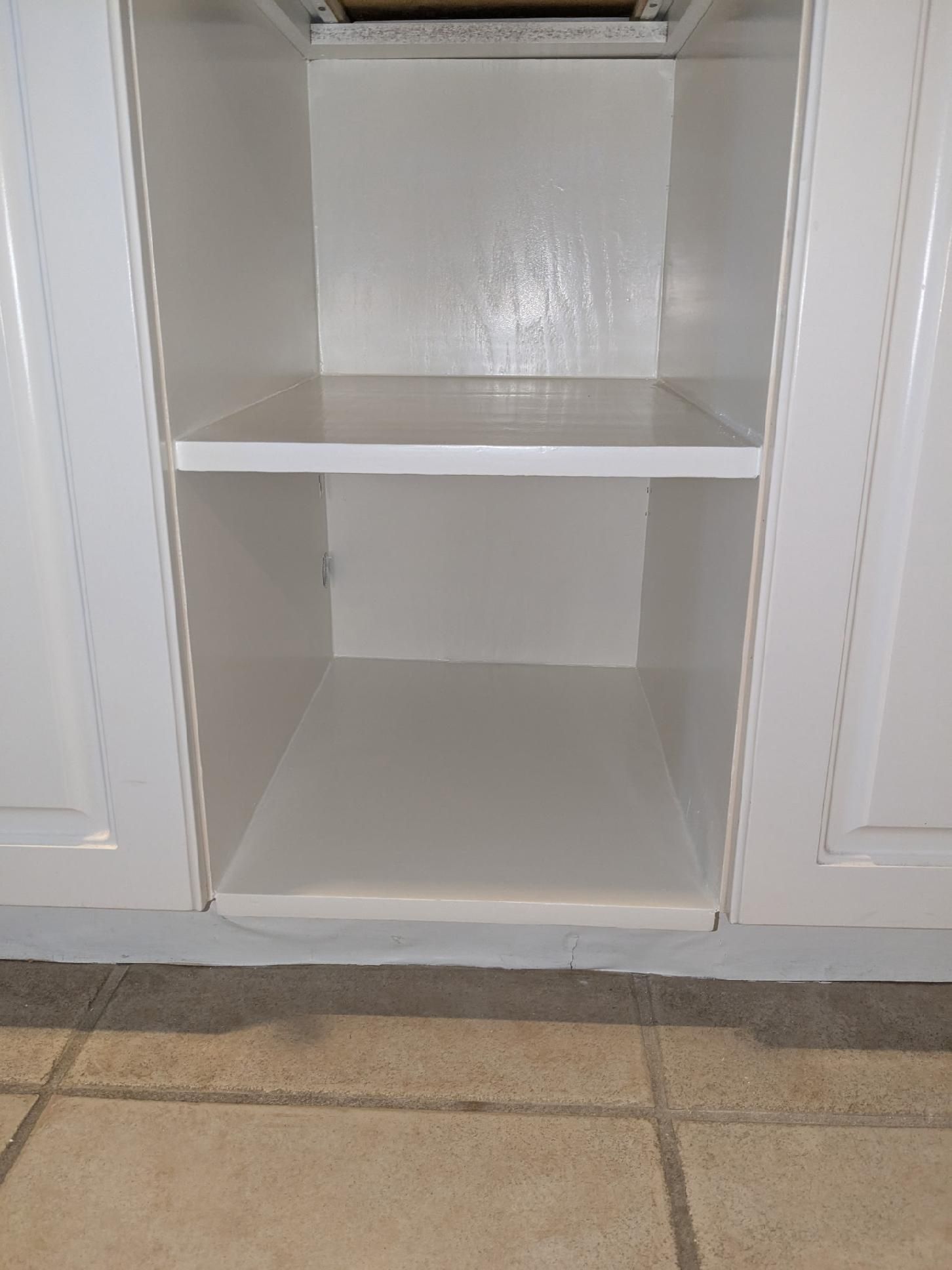 White, empty kitchen cabinet with a shelf. Tile floor.