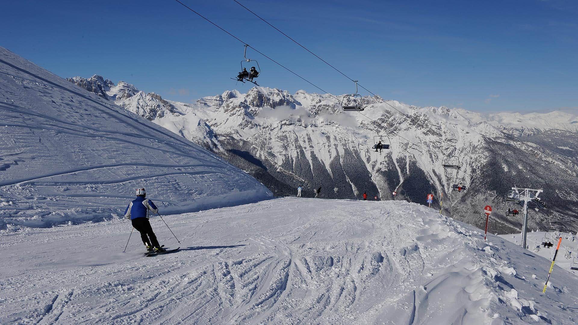 A person is skiing down a snow covered slope with a ski lift in the background.