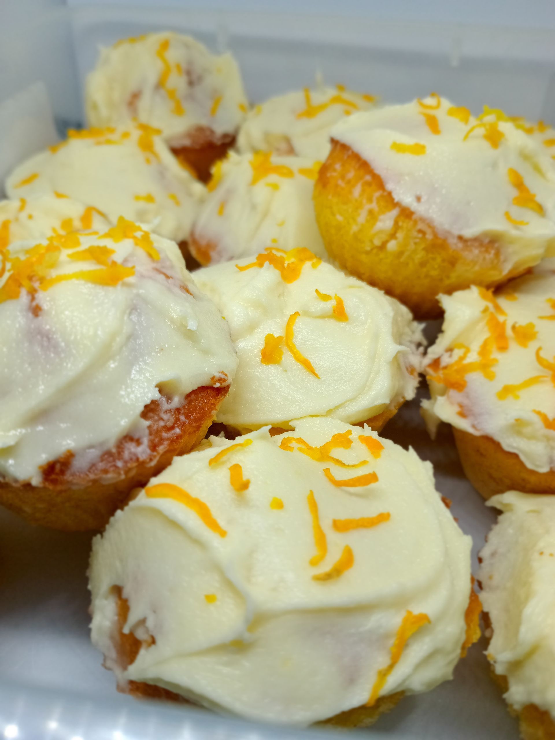 Cupcakes with white frosting and orange zest, piled on a white surface.