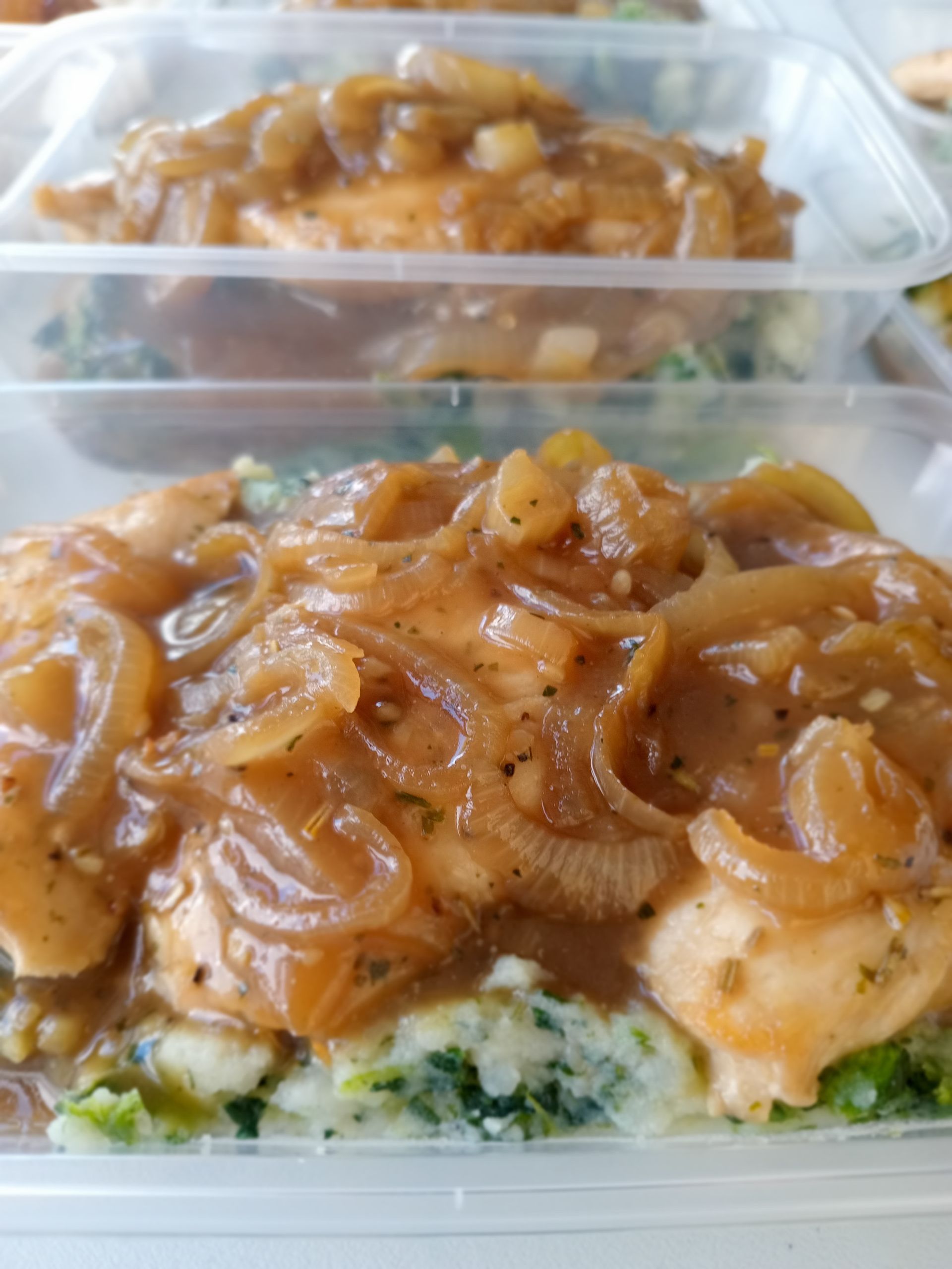 Chicken breasts with onion gravy, served with mashed greens in clear containers.