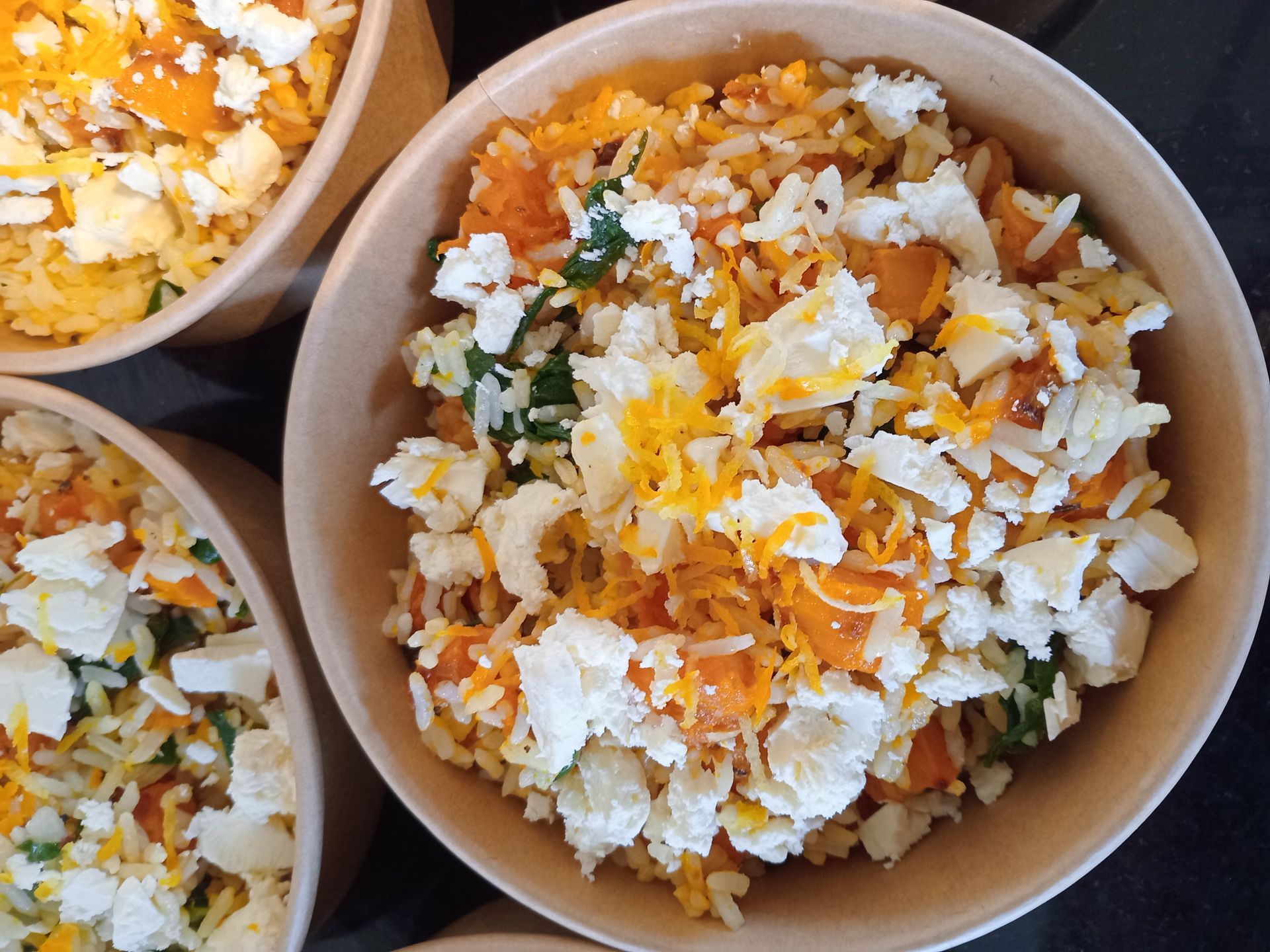 Bowls of rice topped with white cheese, yellow cheese, and orange vegetables.