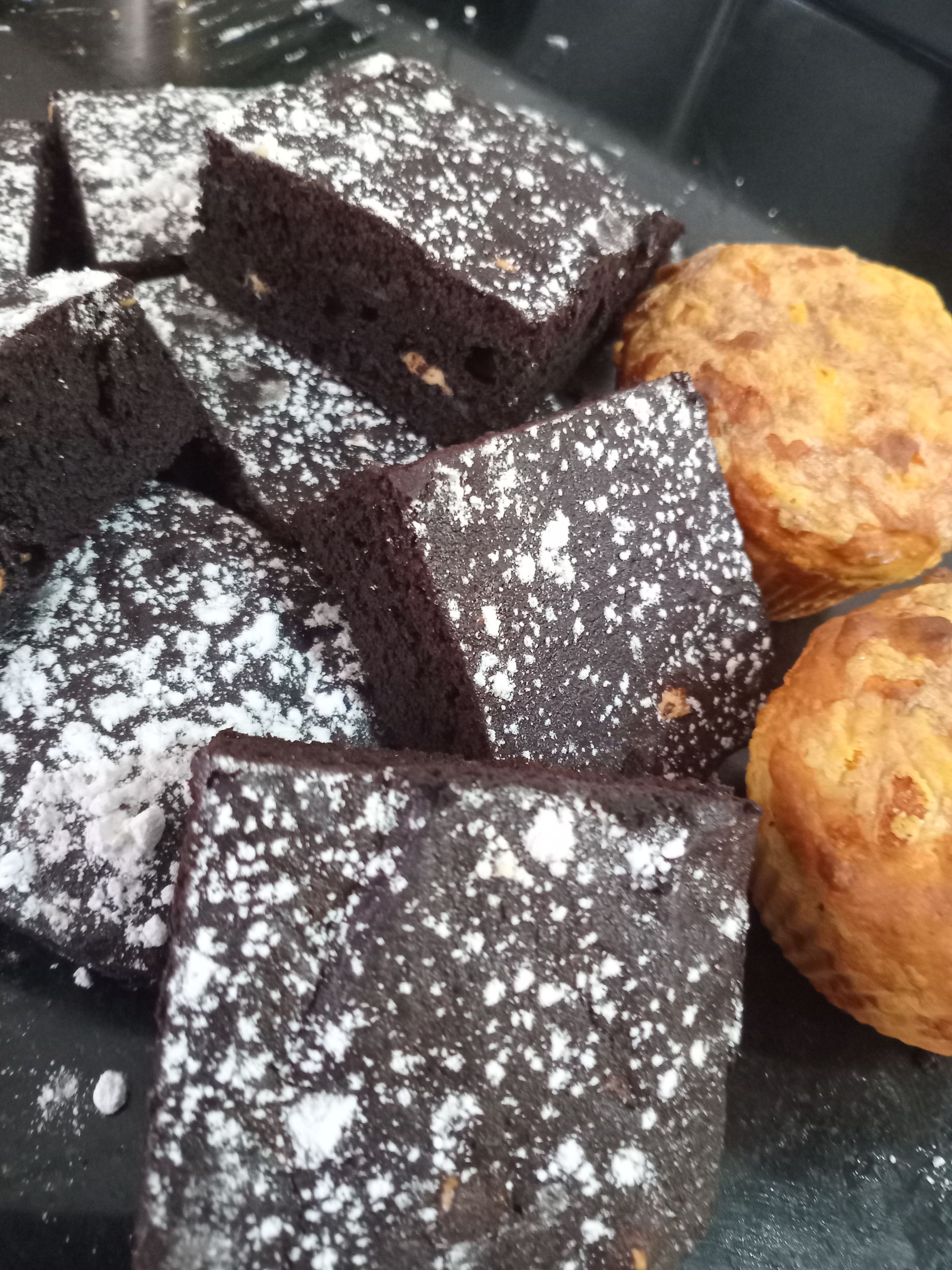 Brownies dusted with powdered sugar; two orange muffins sit nearby.