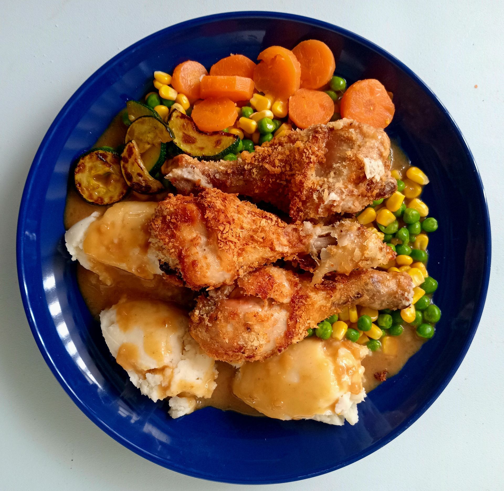 Plate of fried chicken, mashed potatoes, mixed vegetables, and gravy. Blue plate on white.