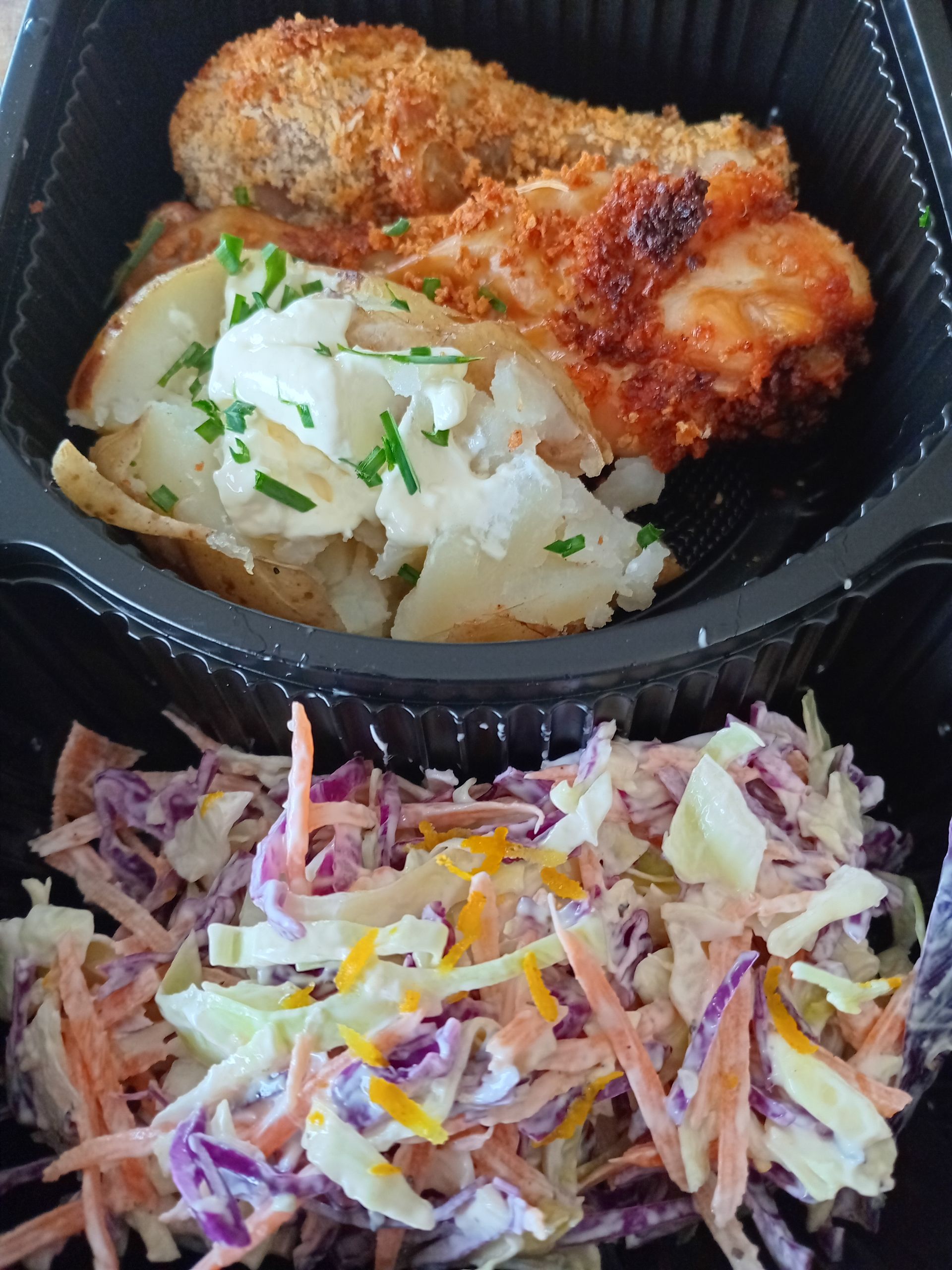 Fried chicken, loaded baked potato, and coleslaw in a black container.