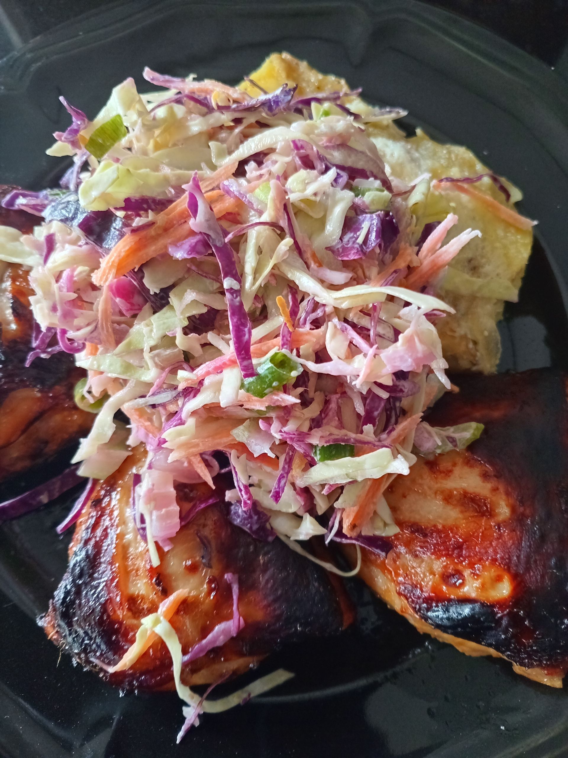 Grilled chicken thighs with slaw and potato salad on a black plate.