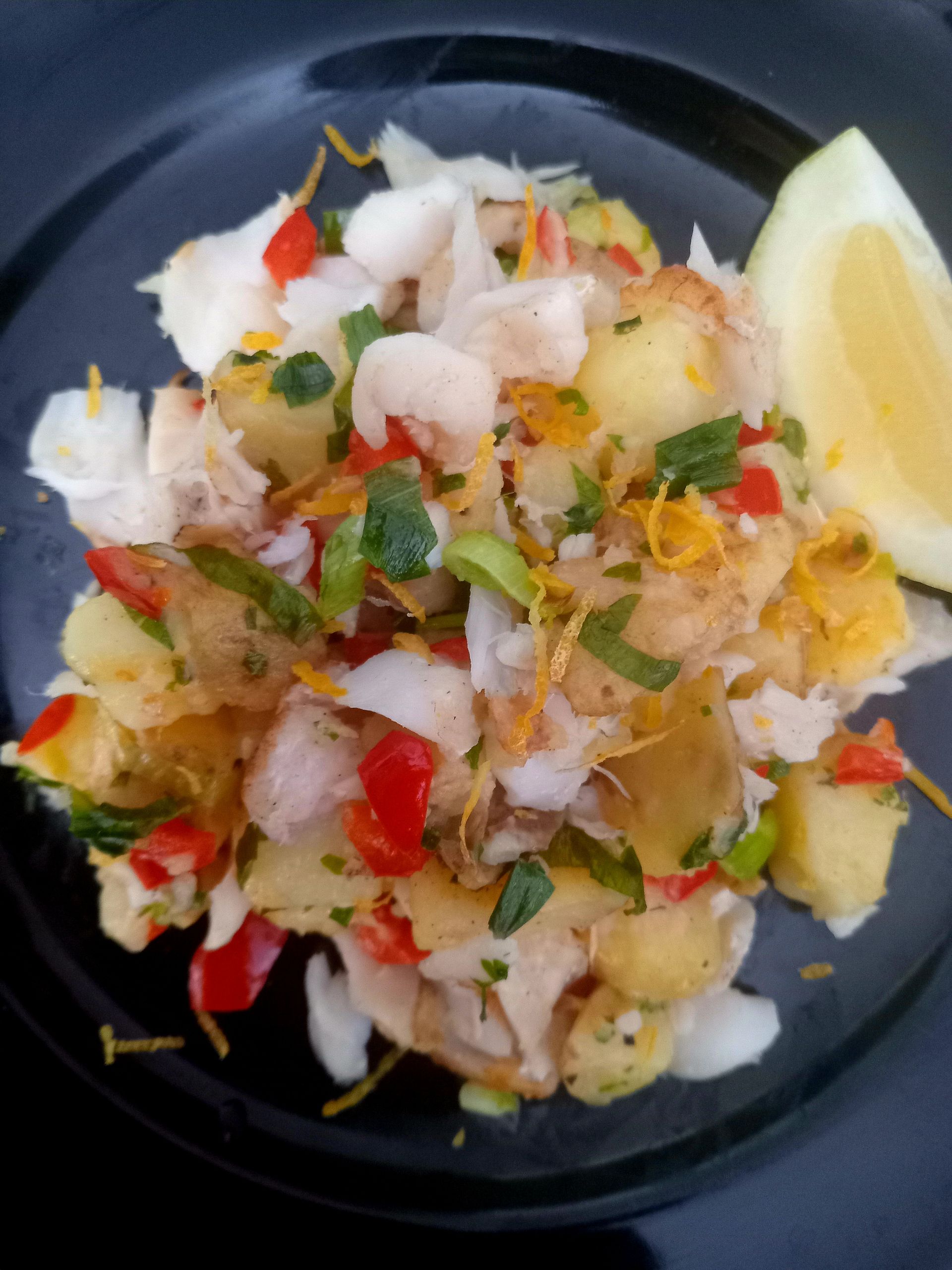 Potato and fish salad with lemon wedge, red peppers, and herbs.