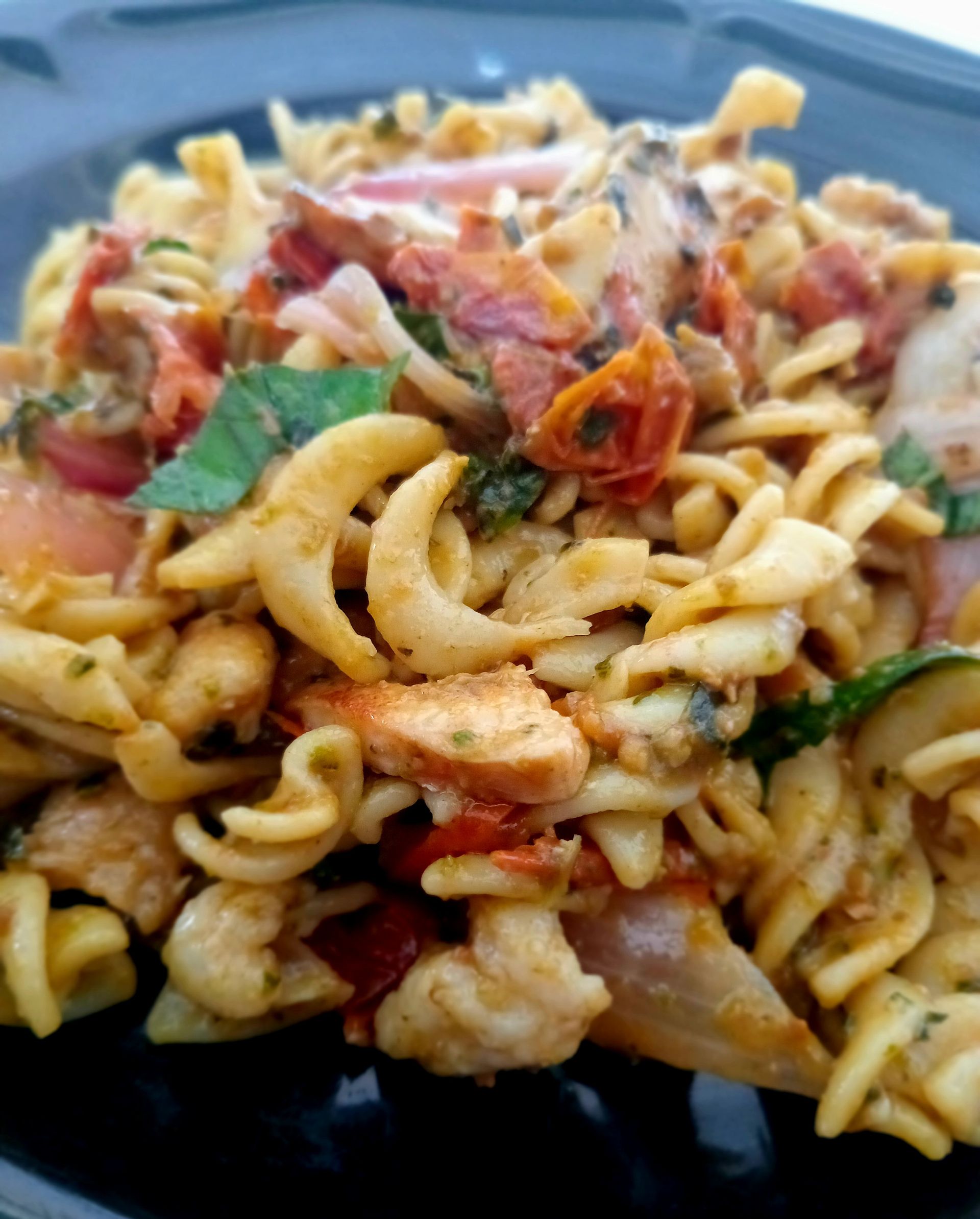 Pasta salad with tomatoes, basil, and zucchini on a black plate.