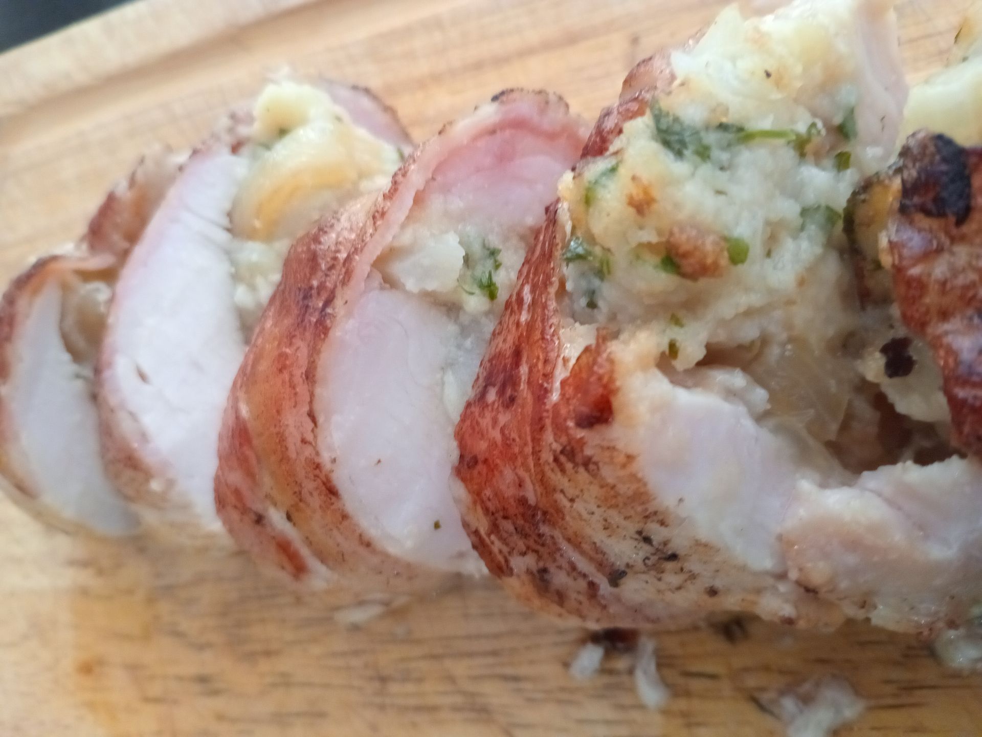 Sliced, bacon-wrapped chicken breast stuffed with stuffing, on a wooden cutting board.