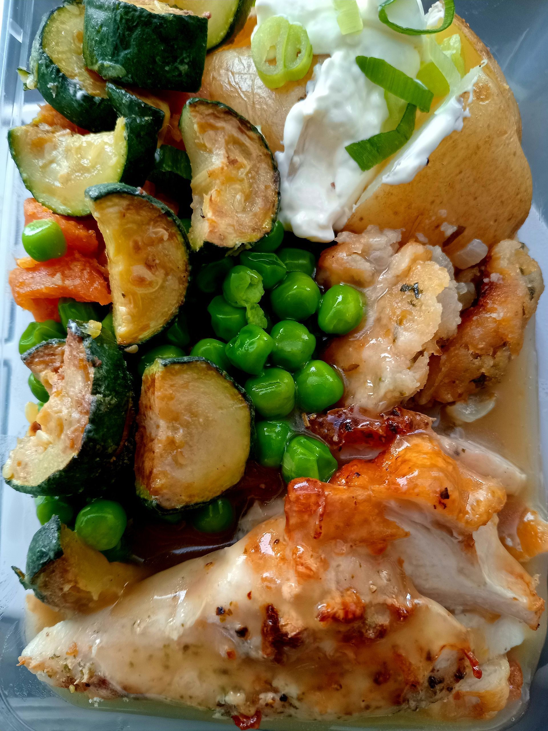 Meal prep container with chicken, vegetables, peas, baked potato with sour cream and green onions.
