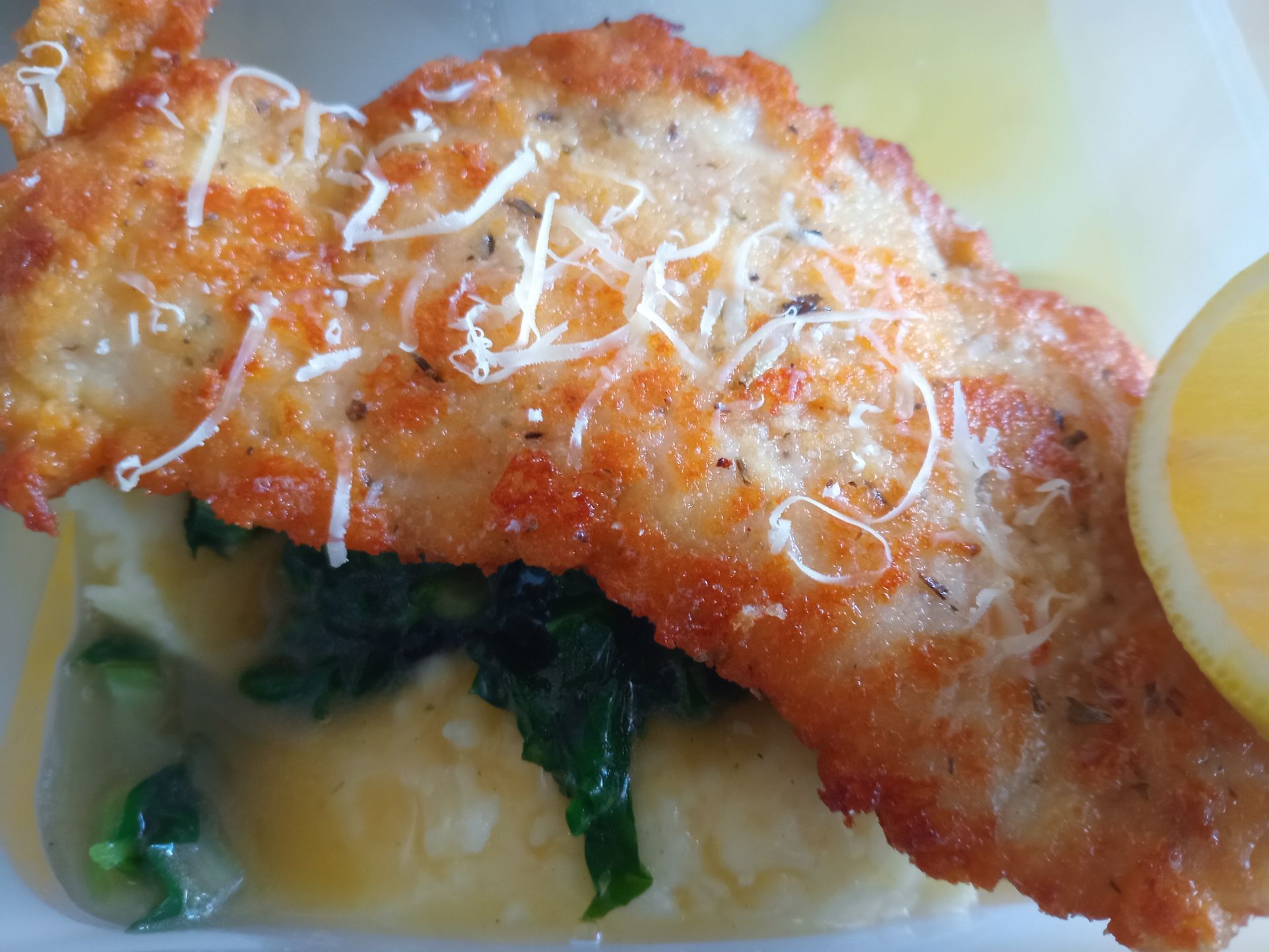 Breaded chicken cutlet with mashed potatoes, spinach, and lemon.