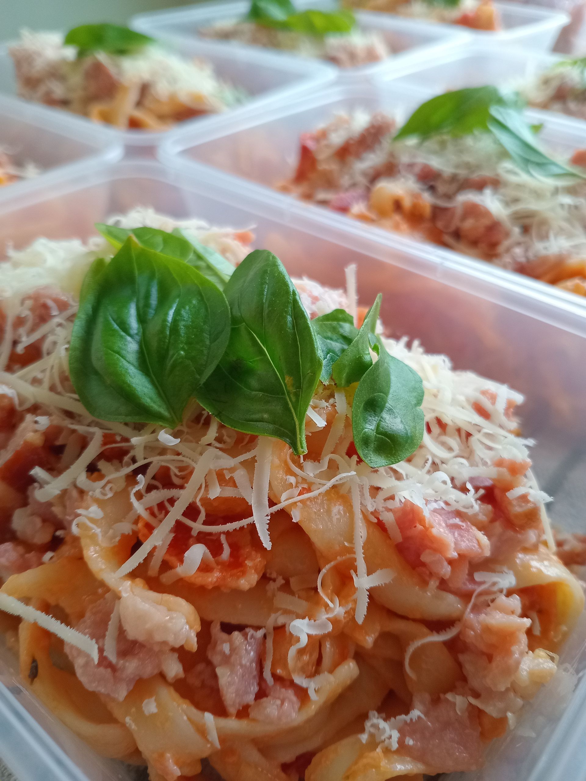 Pasta dish with bacon, cheese, basil, in plastic containers.