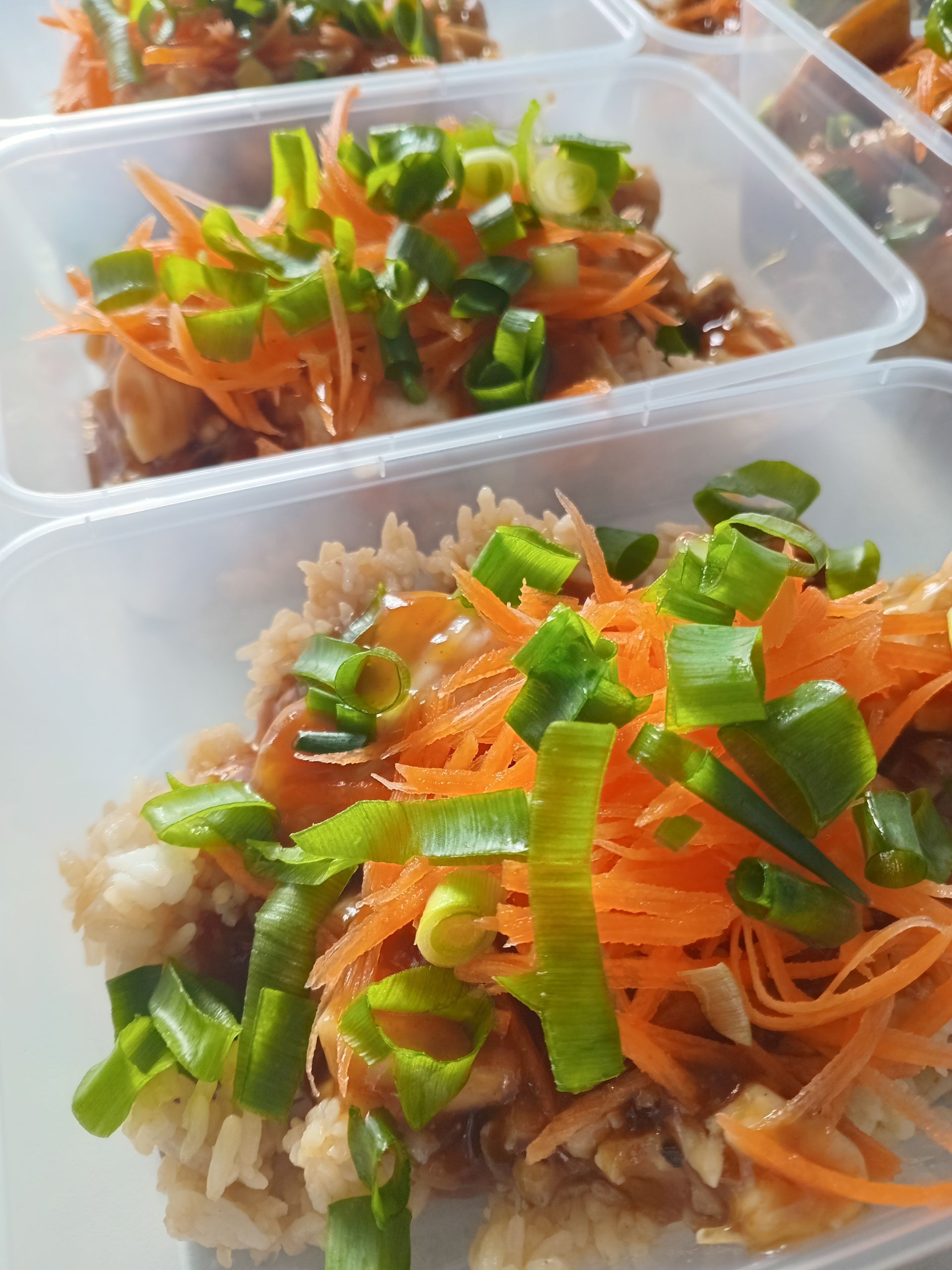 Meal prep containers filled with rice, chicken, carrots, and green onions.