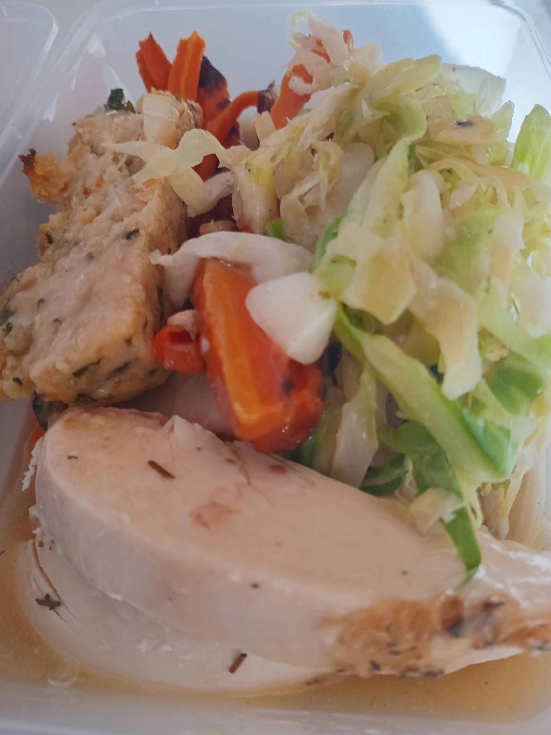 Chicken breast with vegetables and dumpling in a clear container.