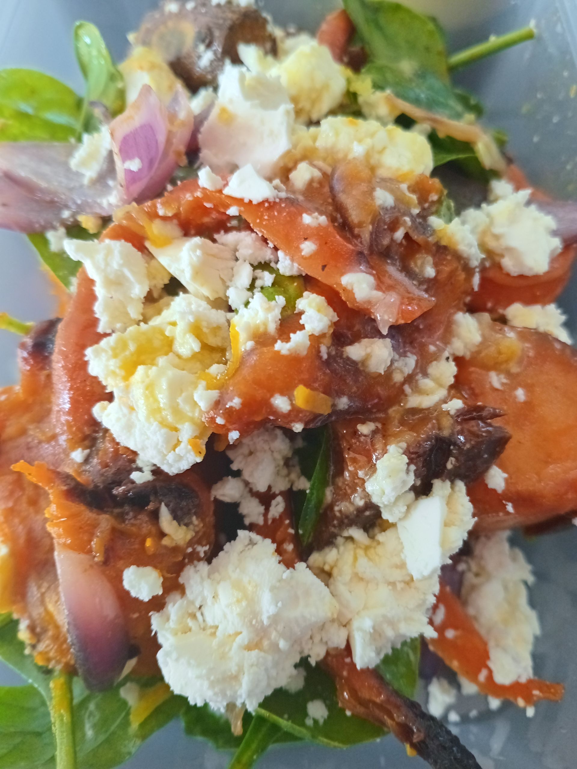 Salad with spinach, red onion, orange vegetables, crumbled white cheese, and dressing.