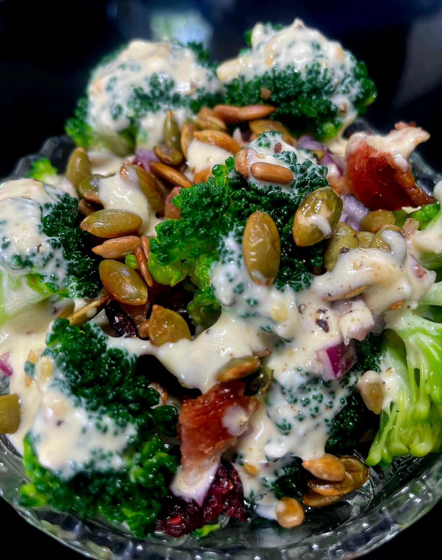 Broccoli salad with creamy dressing, bacon, pumpkin seeds, and red onion in a glass bowl.