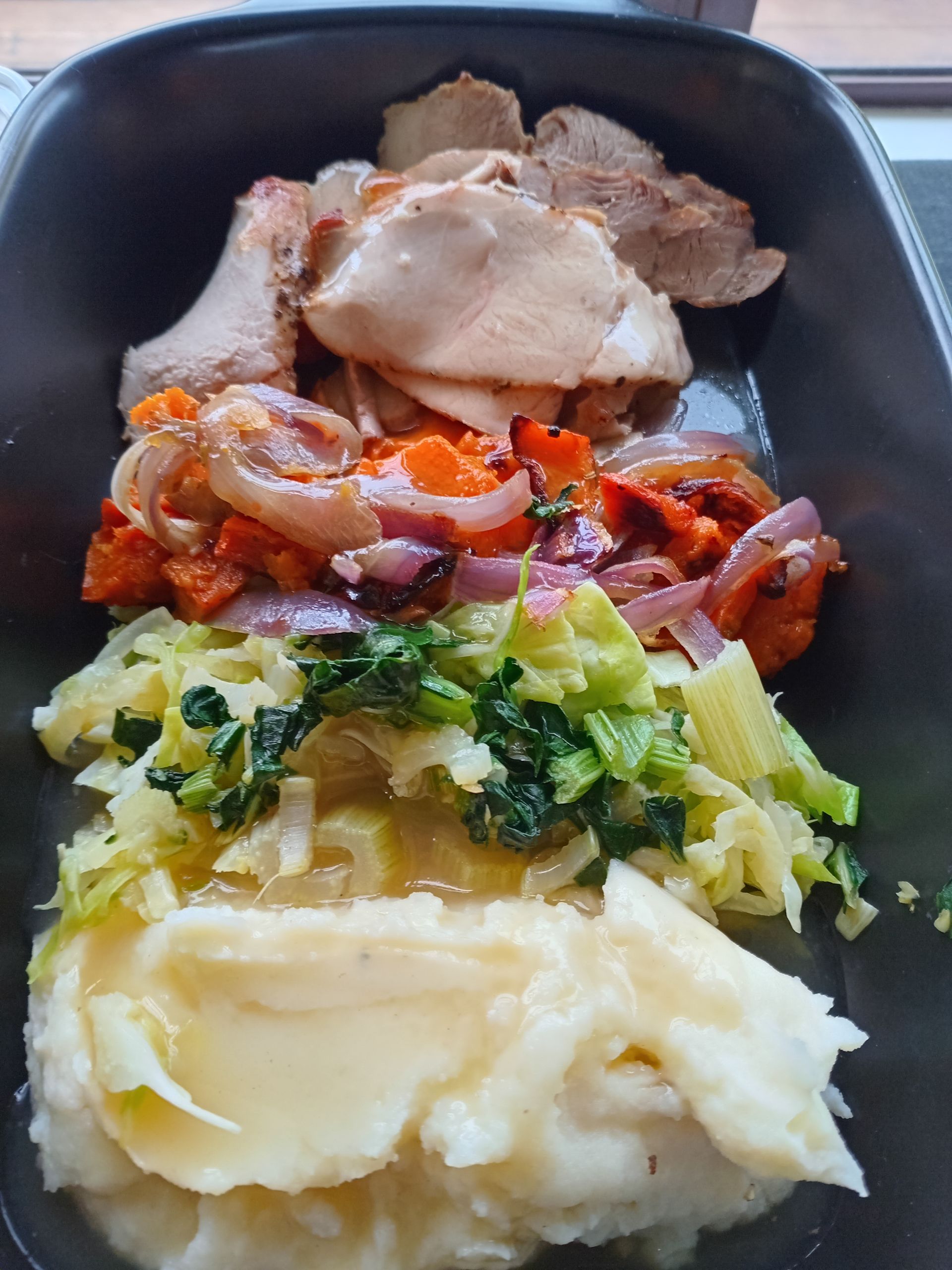 Roasted chicken and vegetables with mashed potatoes in a black tray.