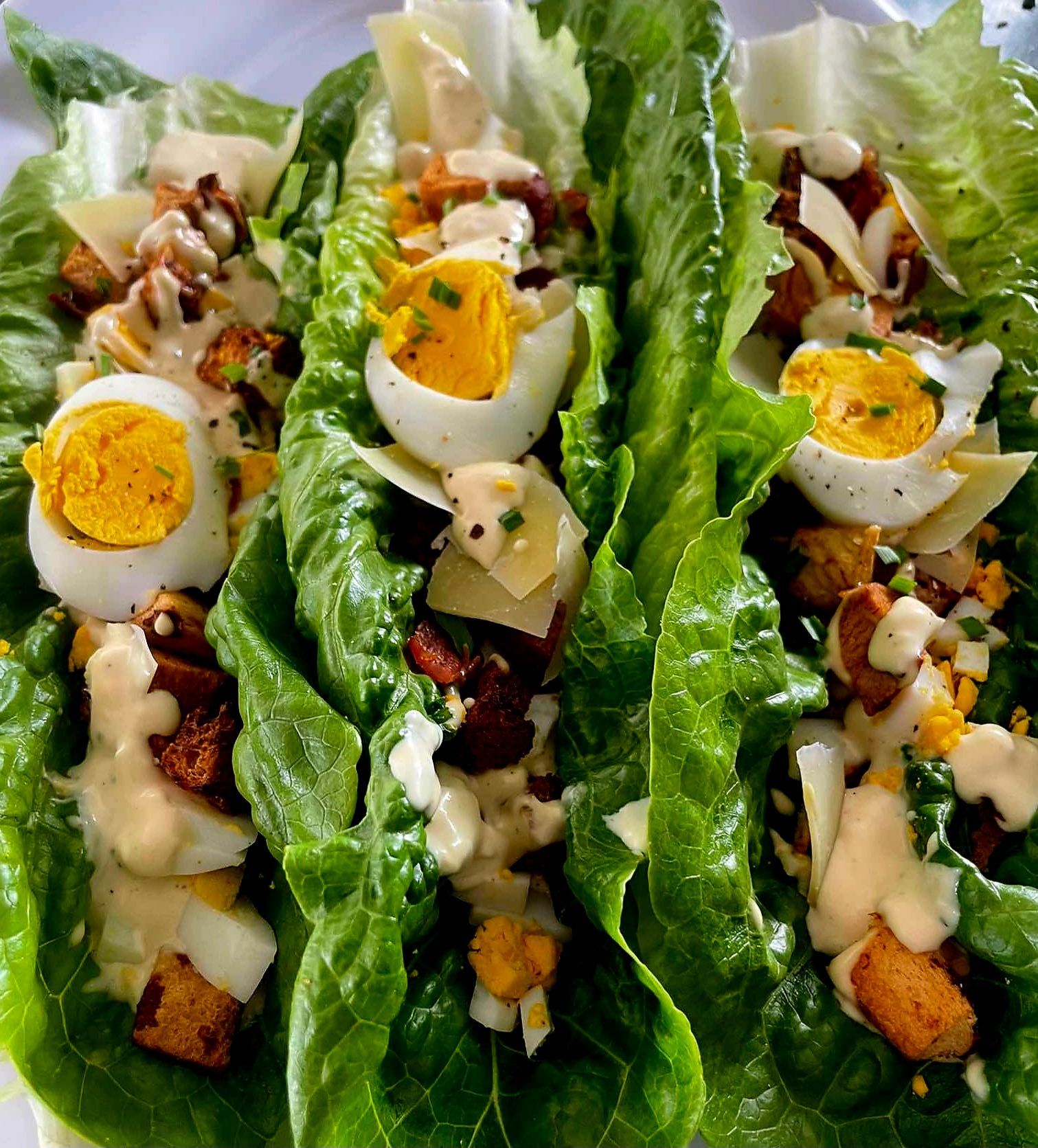 Lettuce wraps filled with Caesar salad ingredients: egg halves, croutons, cheese, and dressing.