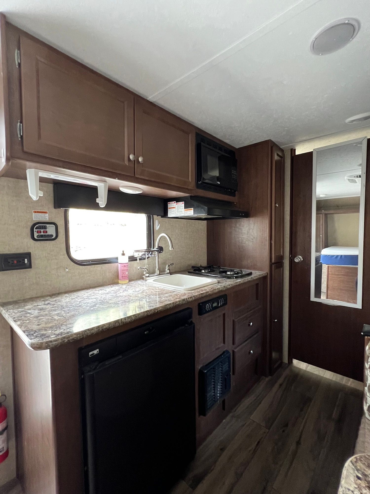 A kitchen in a rv with a sink , stove , refrigerator and microwave.
