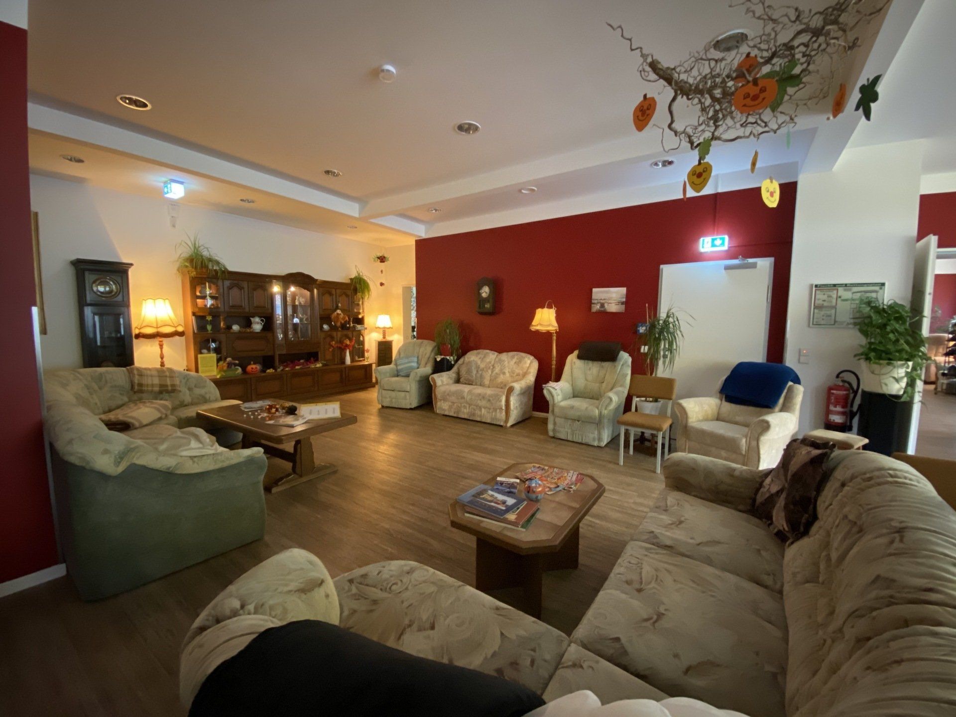 Gemütliches Wohnzimmer mit geblümten Sofas, Sesseln, antiken Möbeln und Herbstdekor; rote Akzentwand.