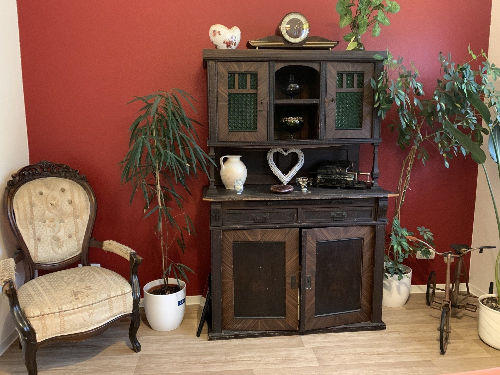 Antiker Holzschrank und Stuhl mit Pflanzen vor einer roten Wand.