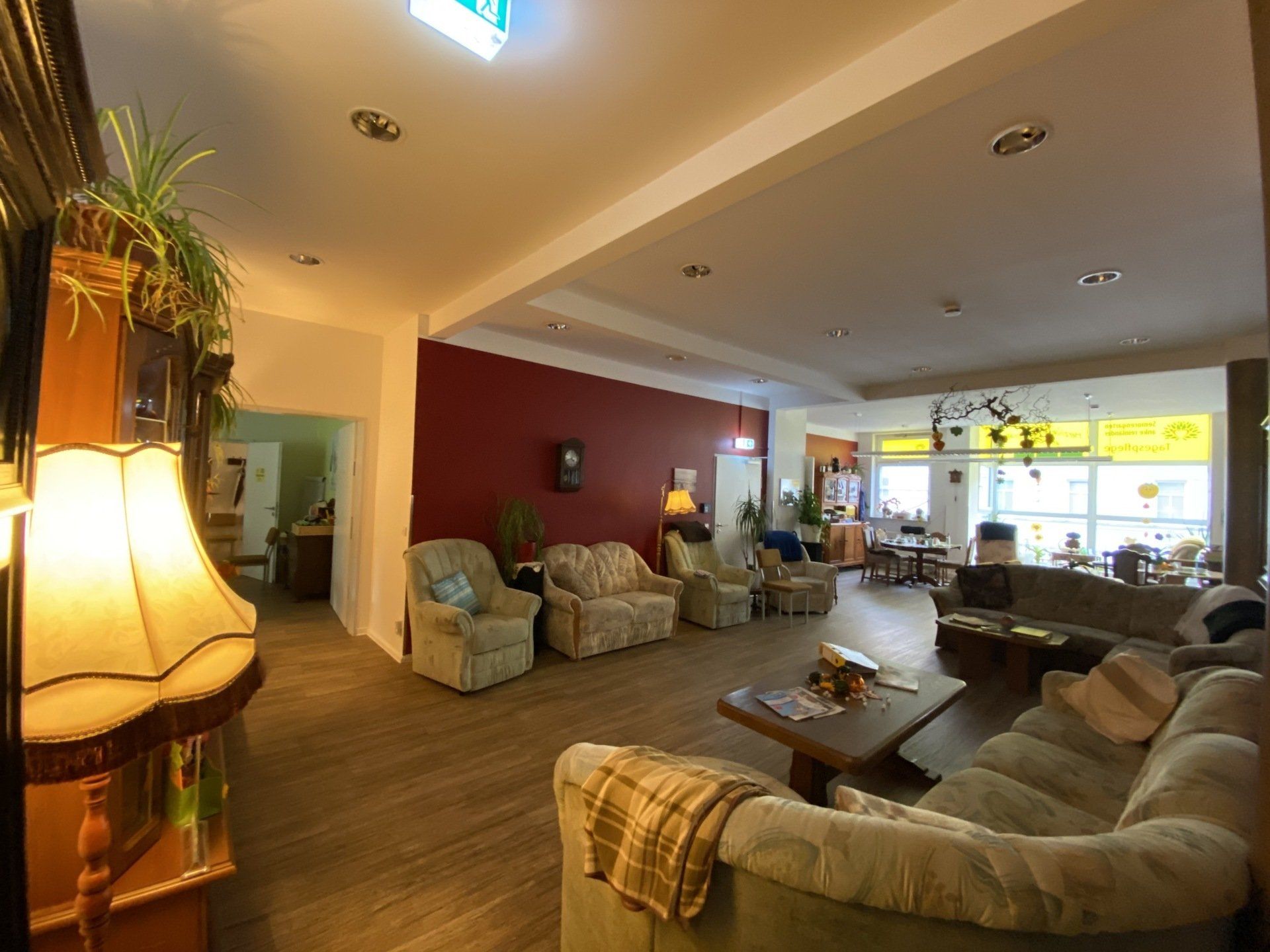 Geräumiger Wartebereich mit Sofas, Sesseln und einem Couchtisch. Rote Akzentwand, Pflanzen und natürliches Licht.