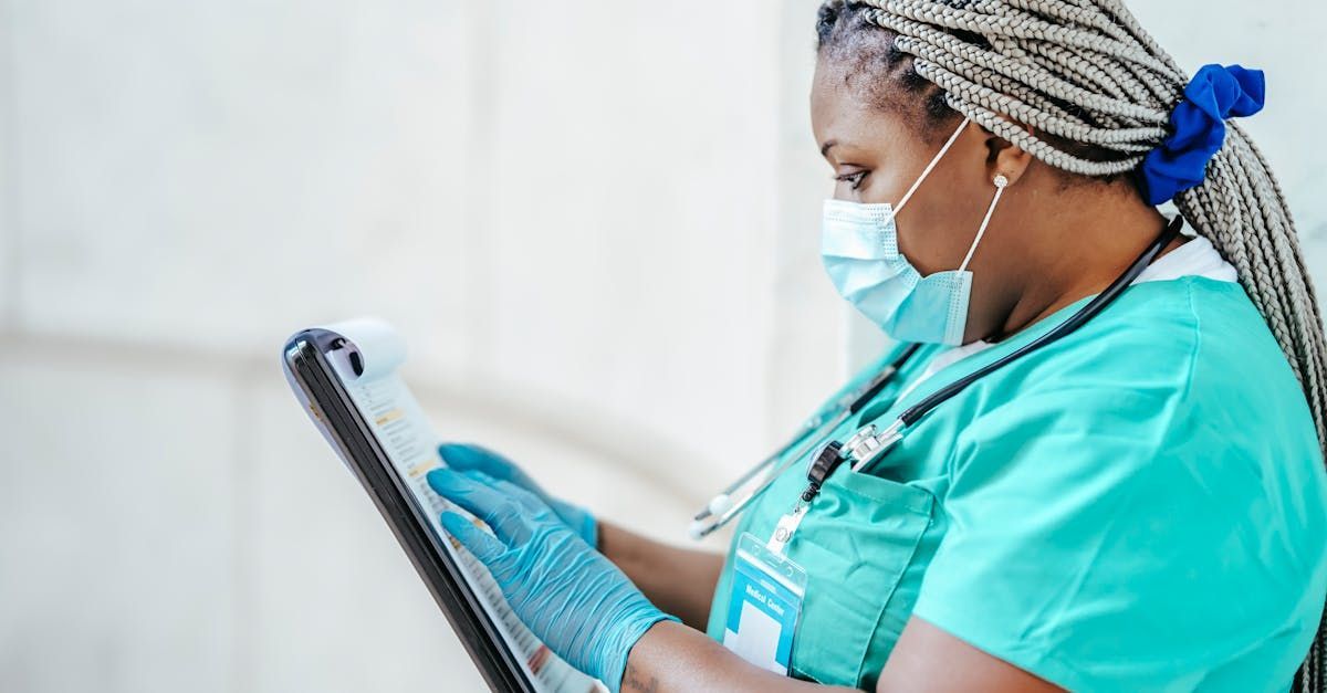 Eine Krankenschwester mit Maske und Handschuhen schaut auf ein Tablet.