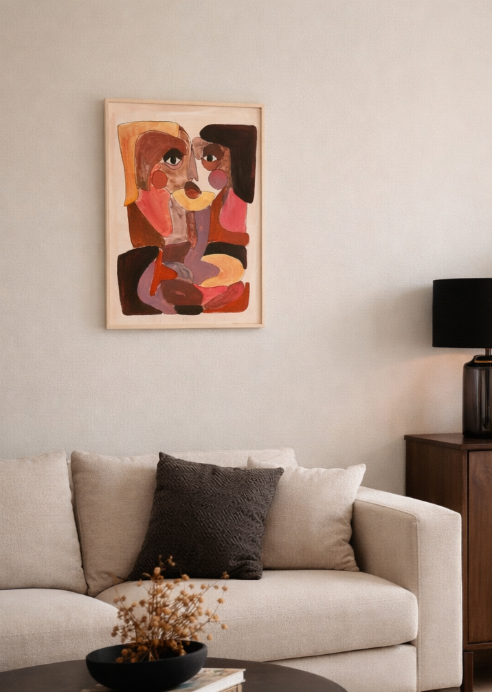 Een abstract schilderij van twee figuren in warme kleuren hangt boven een crèmekleurige bank met een donker kussen.