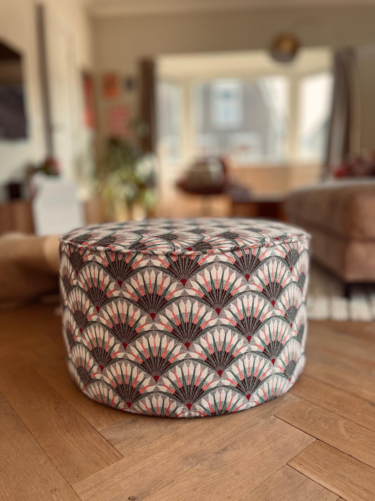 Een ronde poef met een waaiermotief staat op een houten vloer.