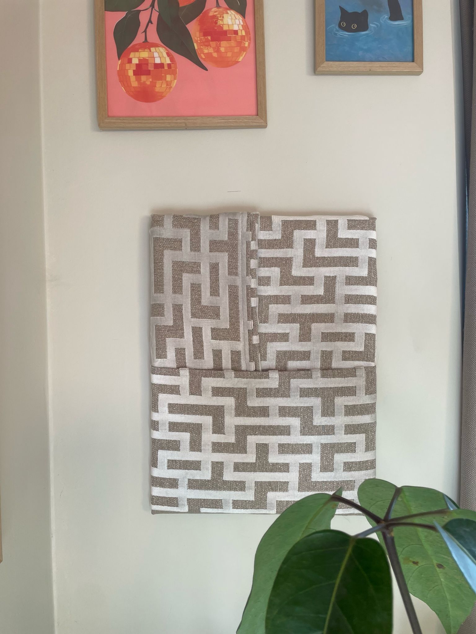 Aan de muur naast een plant hangt een schilderij van een doolhof.
