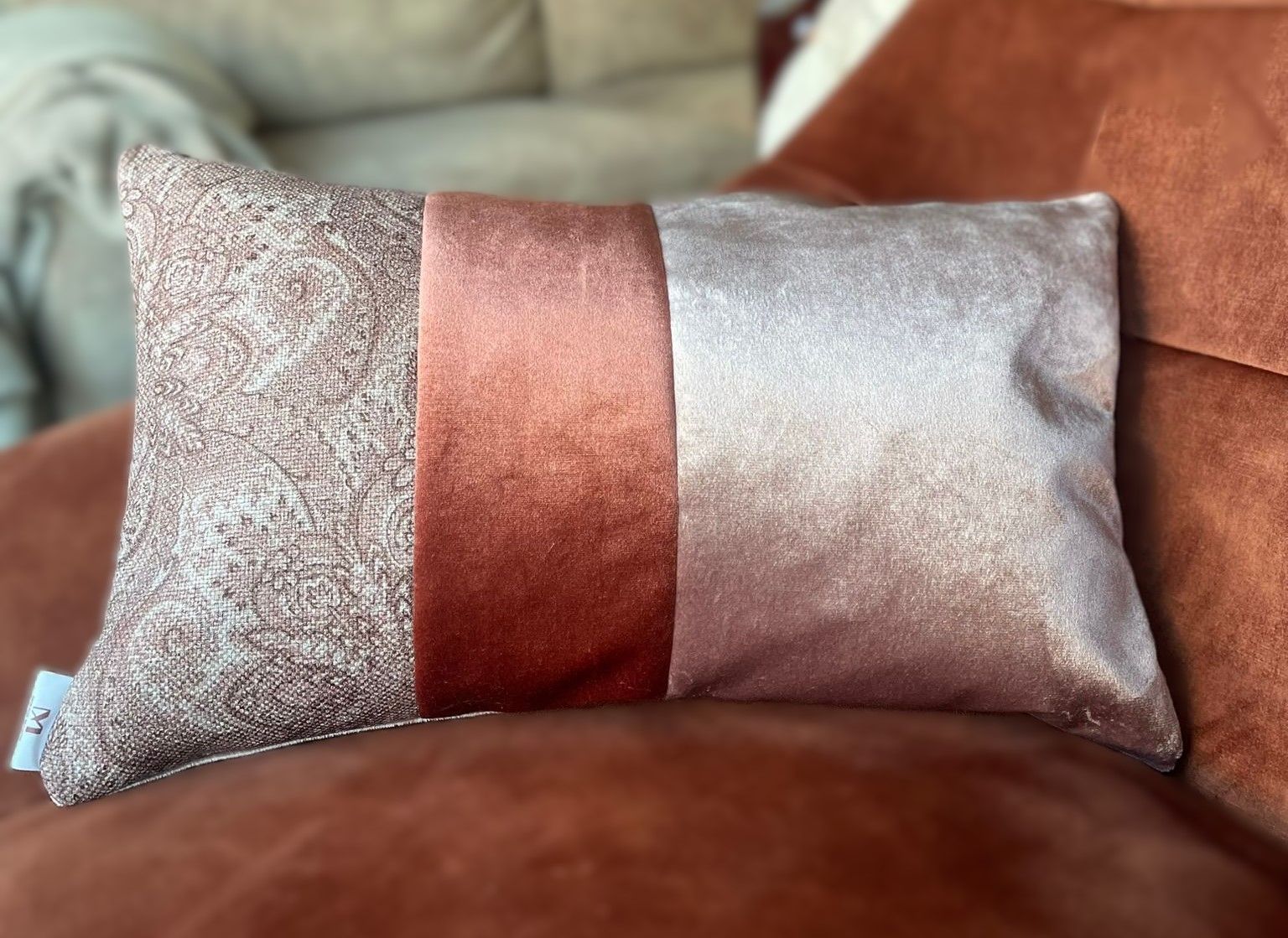 Een kussen met drie secties: een getextureerde bruine laag, roestbruin fluweel en een glinsterende roségouden laag