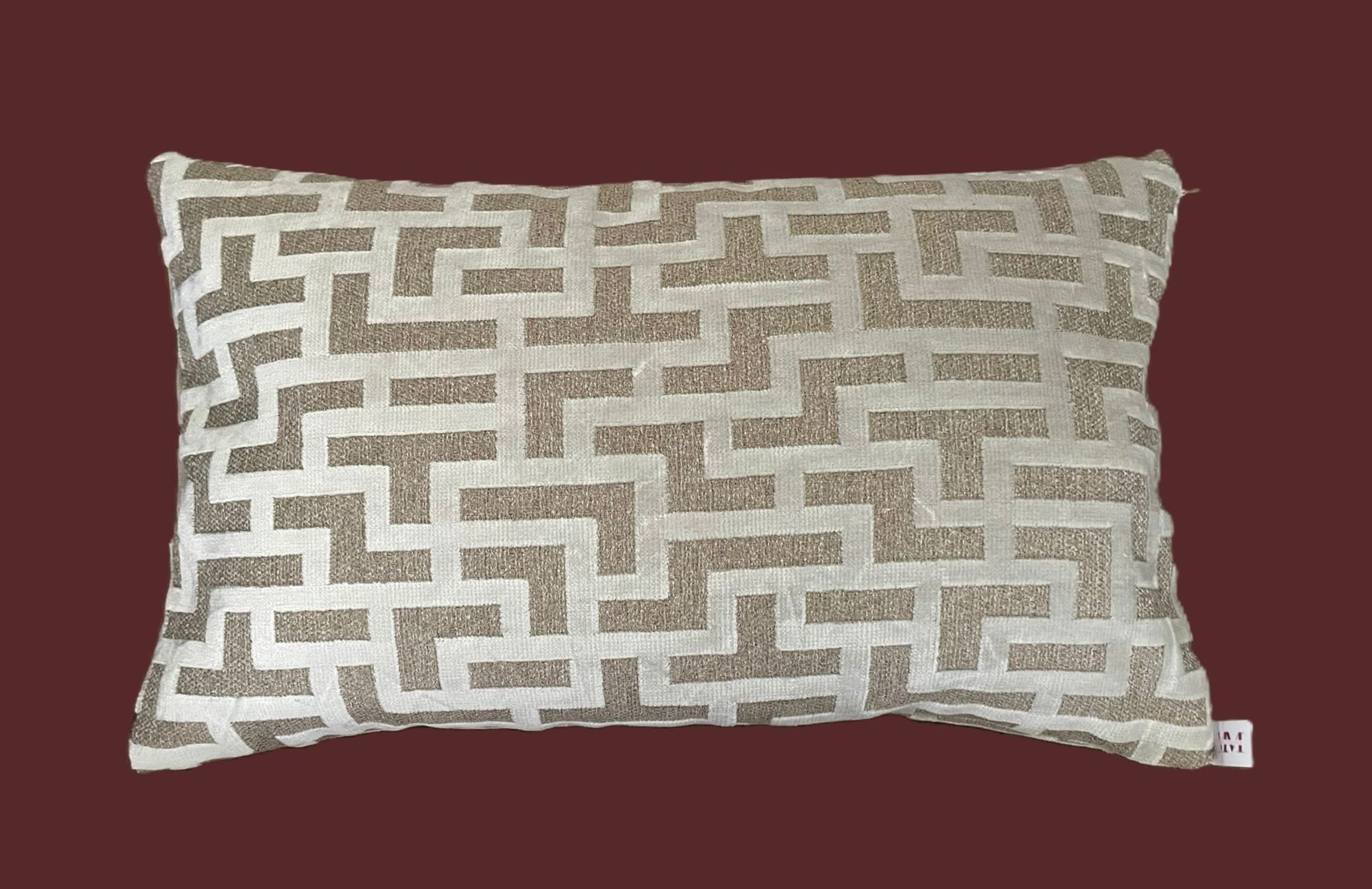 Rechthoekig kussen met geometrisch patroon in crèmekleur en beige op een bruine achtergrond.