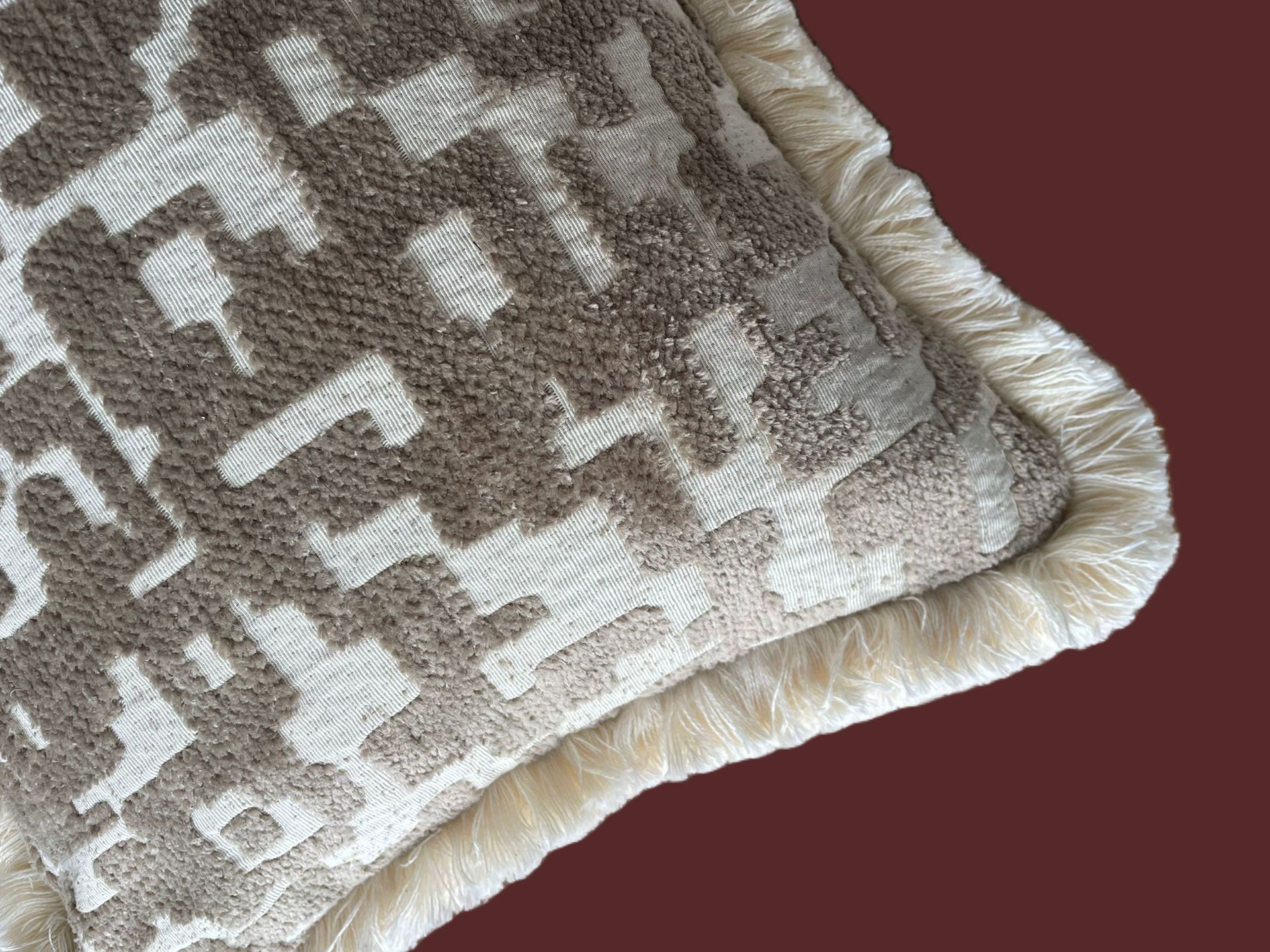 Vierkant kussen met een patroon in beige en crèmekleur, afgewerkt met franjes.