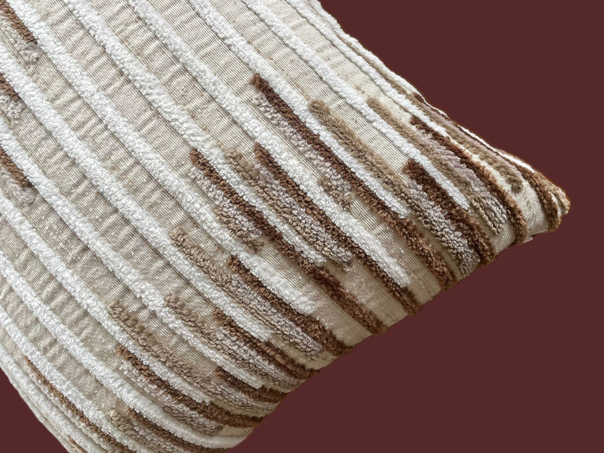 Beige en bruin gestreept kussen met textuur op een bruine achtergrond.