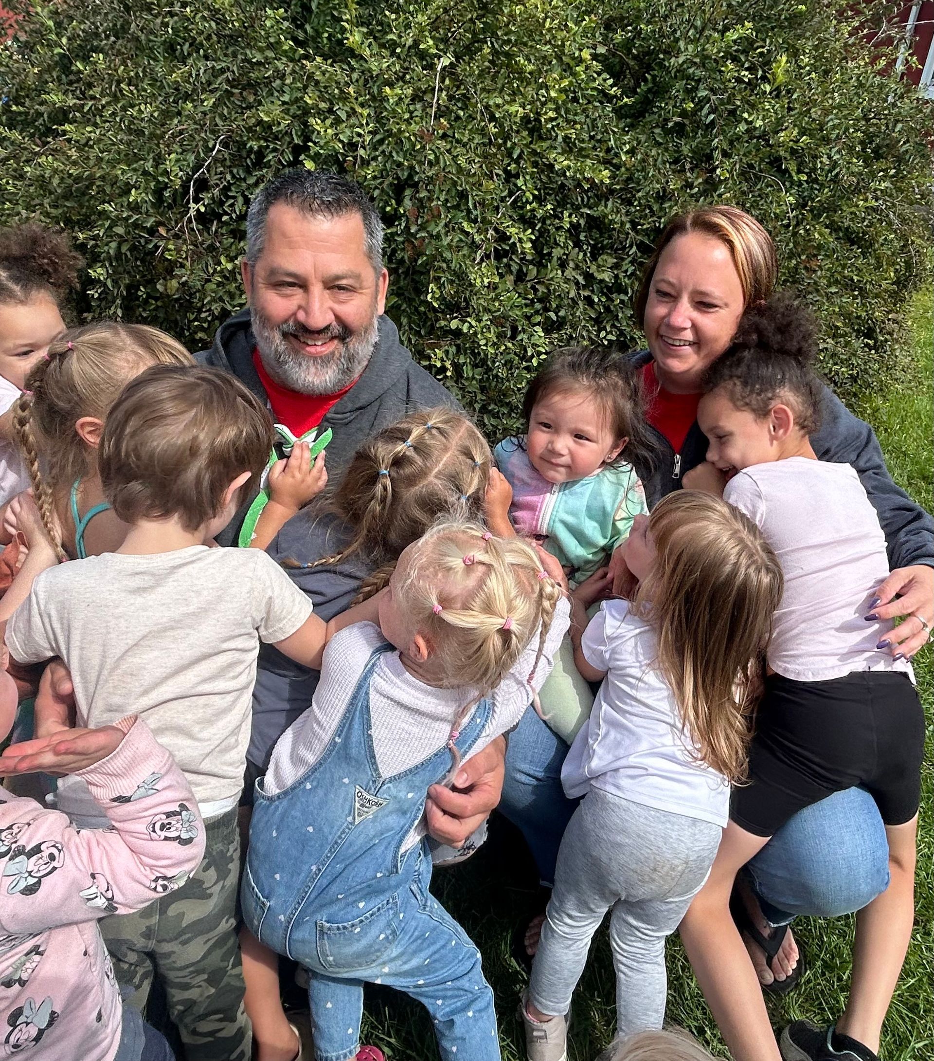 A man and woman are sitting in the grass with a group of children.