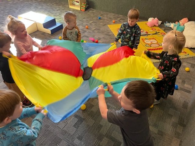 A group of children are playing with a colorful parachute.