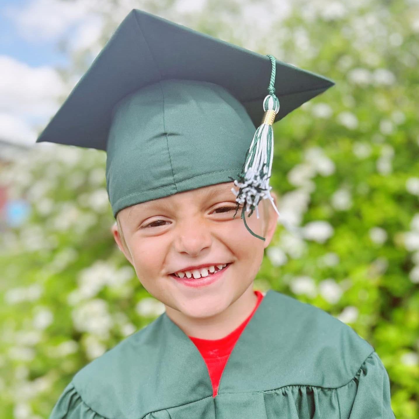 A young boy wearing a graduation cap and gown is smiling