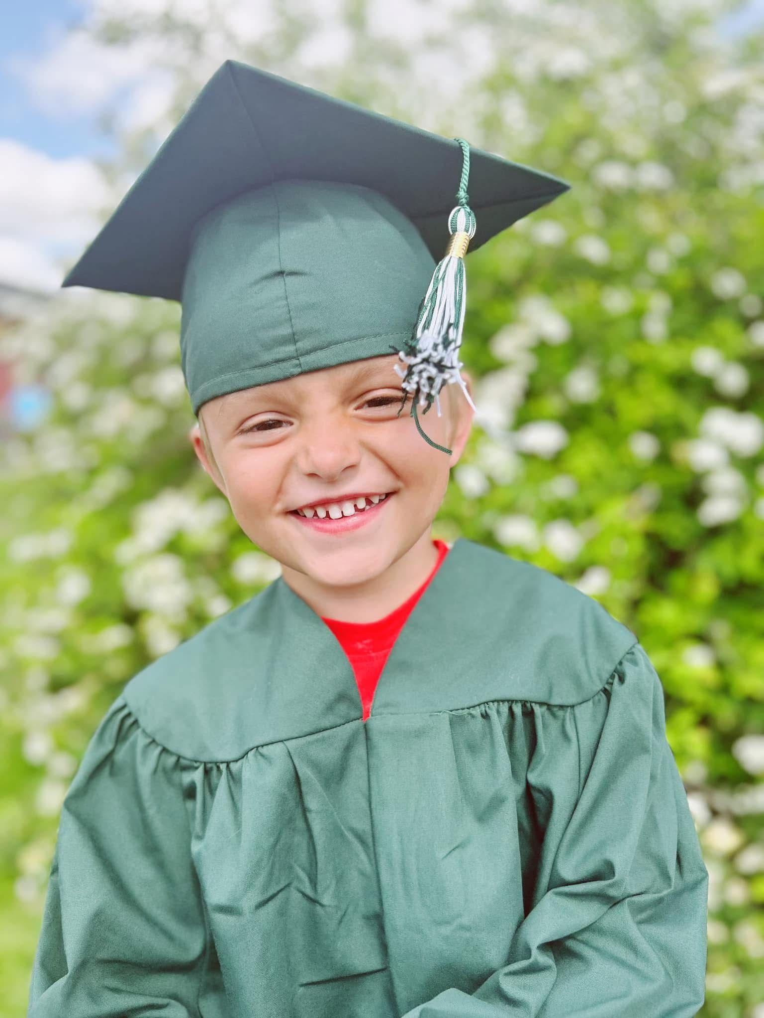 A young boy wearing a graduation cap and gown is smiling