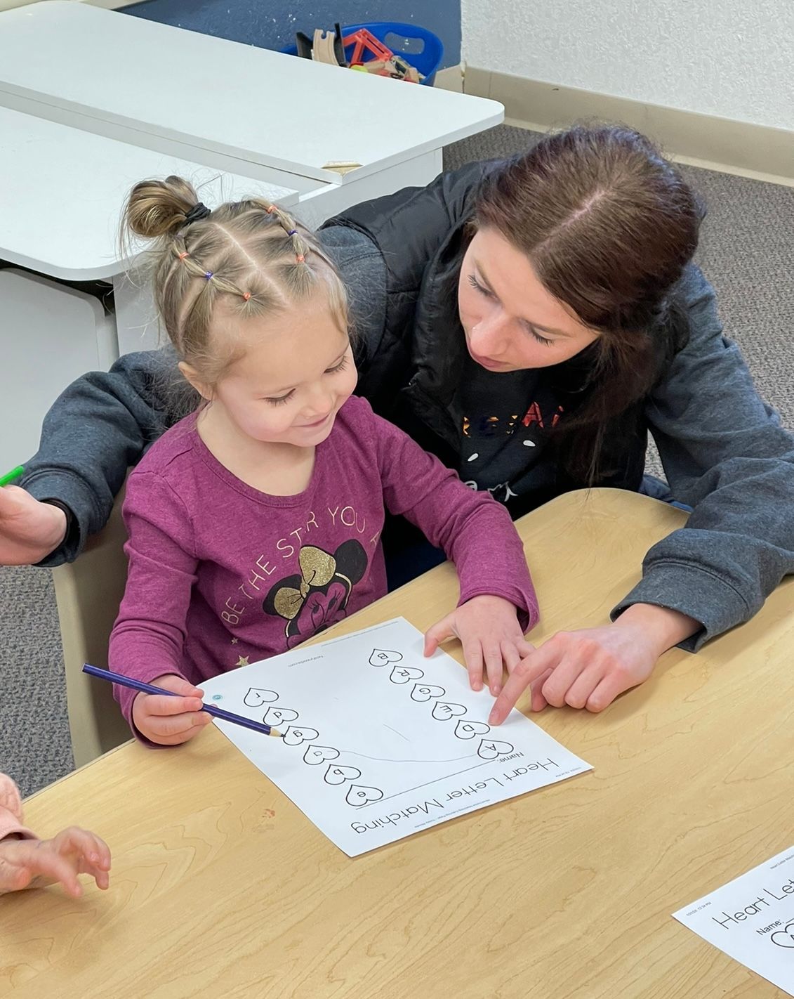 A woman is helping a little girl write on a piece of paper.