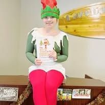A woman dressed as an elf is sitting on a counter holding a book.