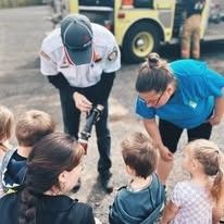 A man is talking to a group of children in front of a fire truck.