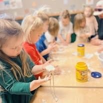 A group of children are sitting at a table playing with clay.