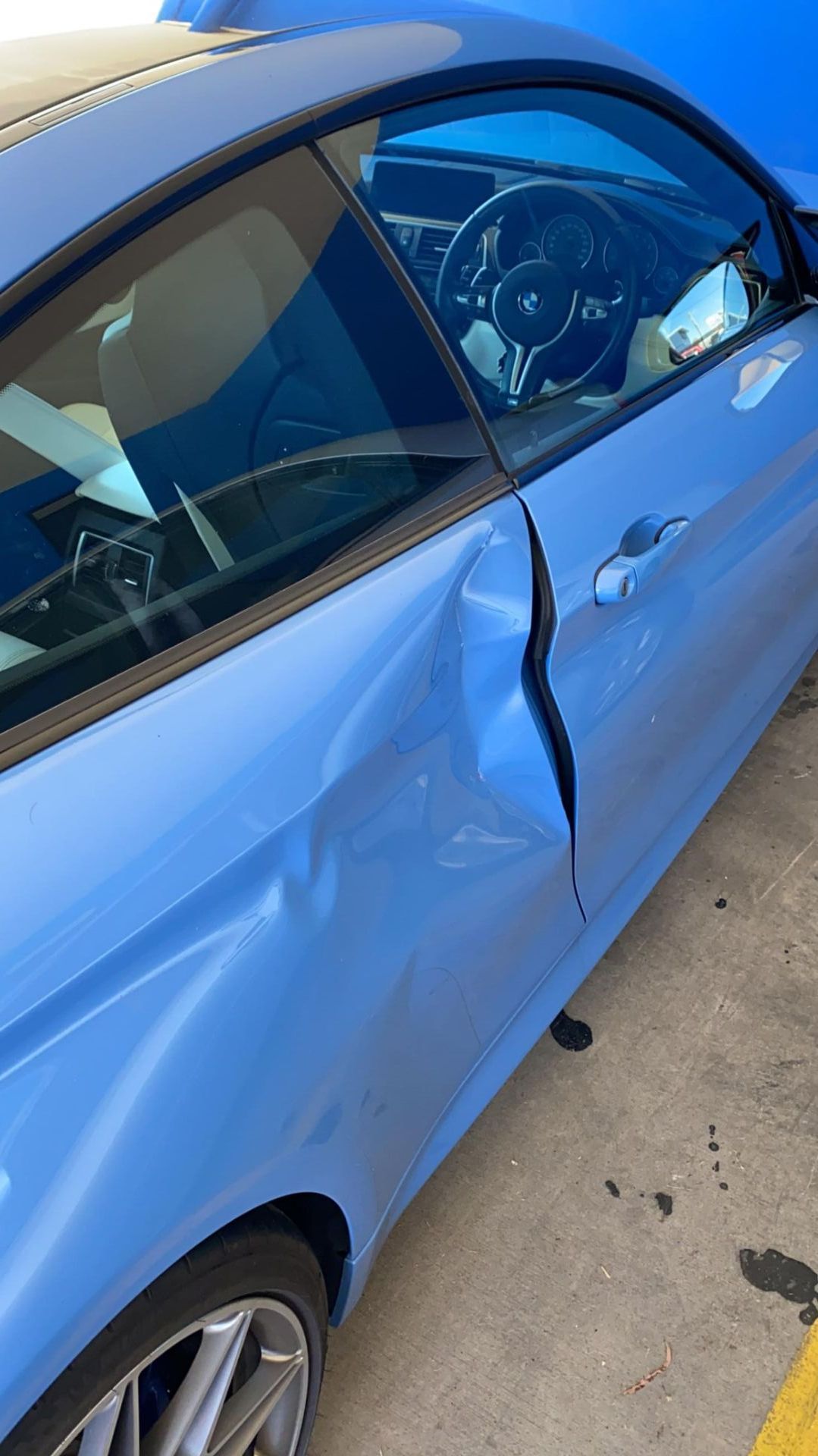 A blue car with a broken door is parked in a parking lot.