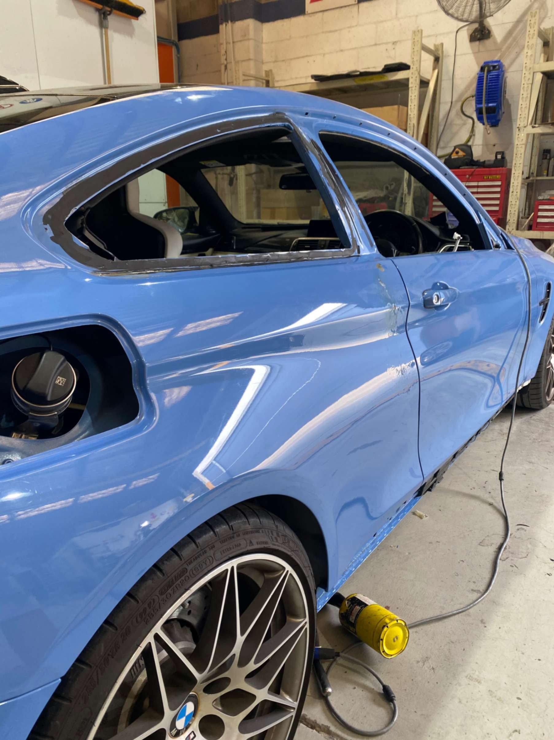 A blue bmw m4 is being worked on in a garage.