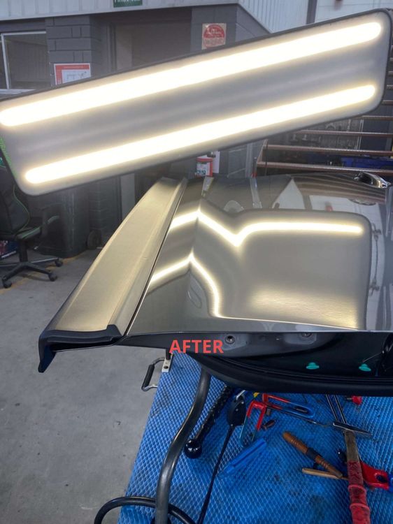 A piece of metal is sitting on top of a table with a light on it after dent removal