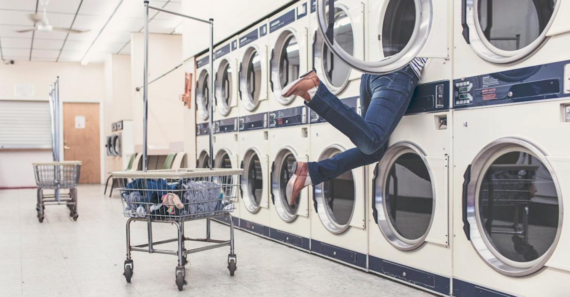 A person is jumping into a washing machine in a laundromat.