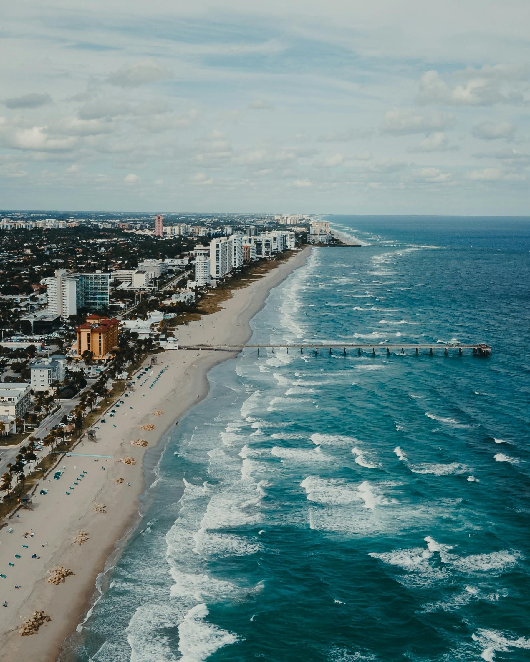 Aerial view of a beachfront city with white sand, turquoise waves, and high-rise buildings along the coast