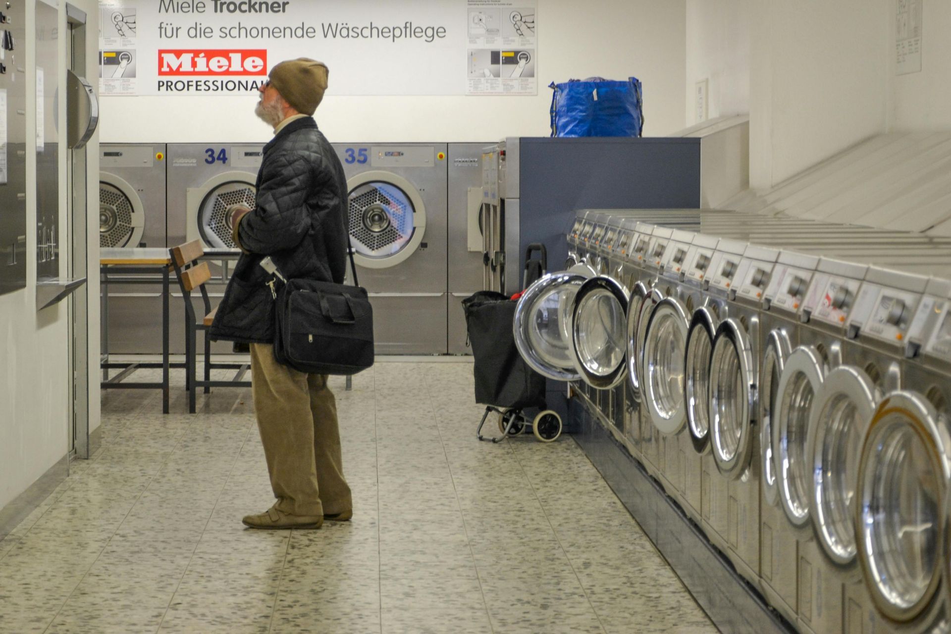 Person standing in a laundromat beside a row of washing machines, looking up at a sign.