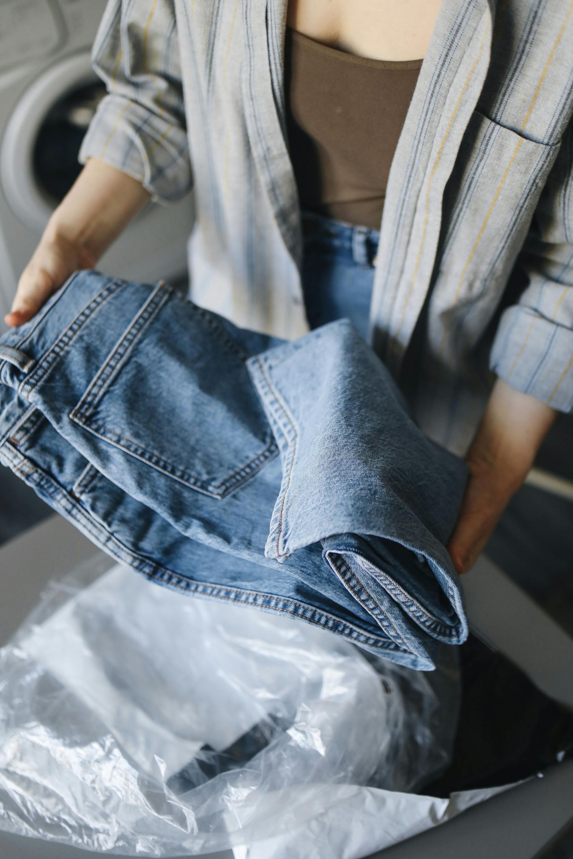 Hands holding folded blue jeans above a plastic laundry bag