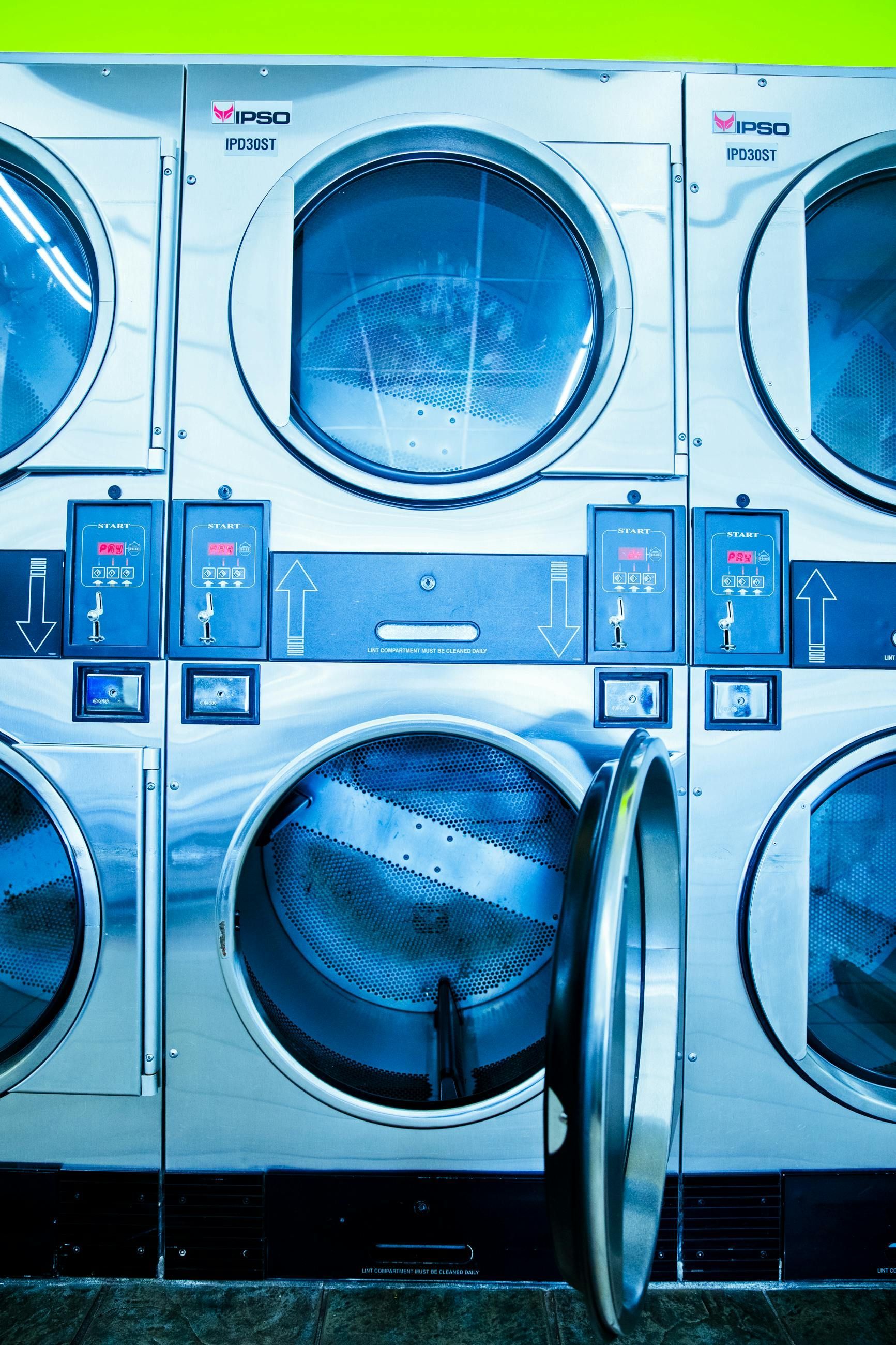 Blue laundromat with stacked front-load washers, one lower machine door open.