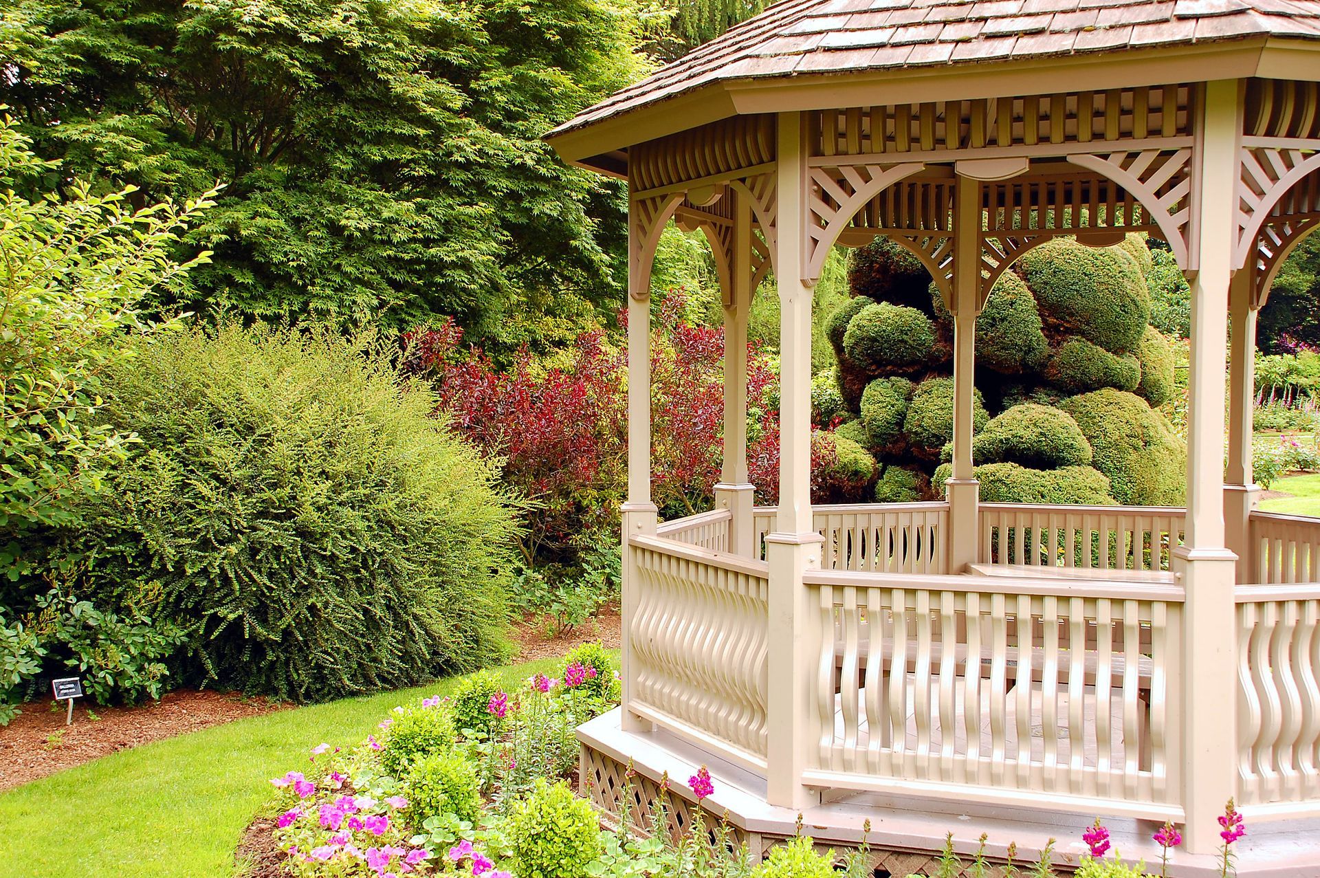 A gazebo in a garden surrounded by bushes and flowers